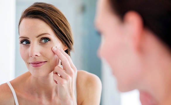 Woman looking in the mirror at her skin improvements from ASEA Renu 28 Redox Gel