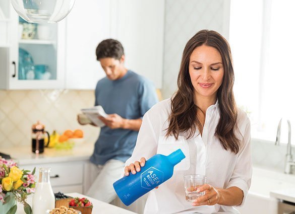 Young looking couple in their kitchen where woman in pouring ASEA supplement into glass